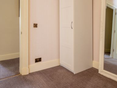 A corner of a room with a white wardrobe beige patterned wallpaper and a large ornate mirror at Silverholme Graythwaite near Hawkshead