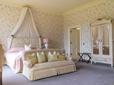 A bedroom with a bed canopy sofa with pillows mirrored wardrobe and suitcase rack at Silverholme in Graythwaite near Hawkshead