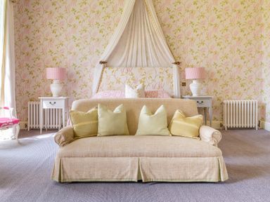 A bedroom with a sofa and pillows facing a bed with a canopy and bedside tables with lamps at Silverholme in Graythwaite near Hawkshead