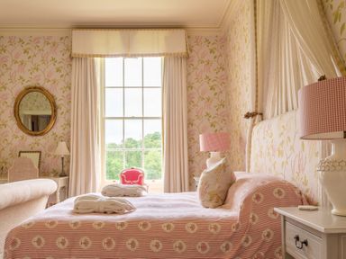 A bedroom with a bed covered in pink patterned bedding with two robes on it and a large window with curtains at Silverholme in Graythwaite near Hawkshead
