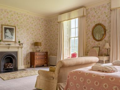 A bedroom with a floral wallpaper fireplace wooden chest of drawers sofa bed with pink bedspread and window at Silverholme Graythwaite near Hawkshead