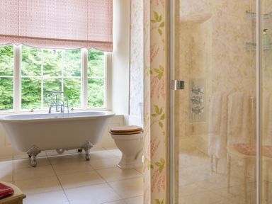 A bathroom with a freestanding bathtub beside a window a toilet with a wooden seat and a glass shower enclosure at Silverholme in Graythwaite near Hawkshead