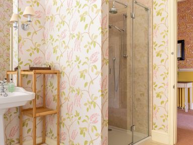 A bathroom with a floral wallpaper a wooden shelf a sink and a glass shower at Silverholme Graythwaite near Hawkshead