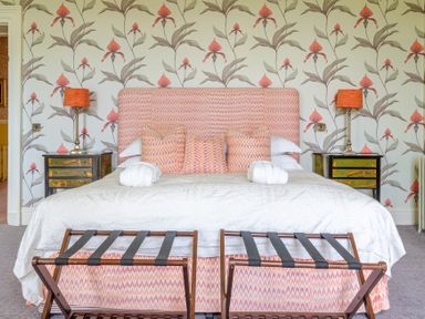 A bedroom with a bed with patterned pillows and headboard two bedside tables with lamps and luggage racks at Silverholme Graythwaite near Hawkshead