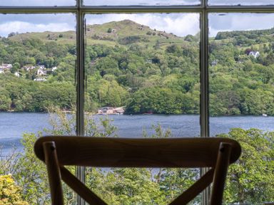 A wooden chair in front of a window overlooking a lake hills and houses at Silverholme in Graythwaite near Hawkshead