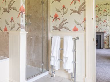 A bathroom with a glass shower enclosure white towels on a heated towel rail and floral wallpaper at Silverholme Graythwaite near Hawkshead