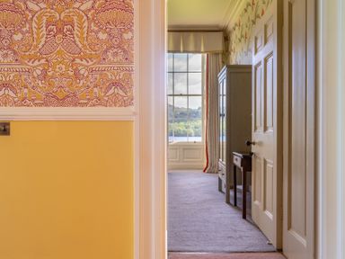 A hallway leading to a room with a window showing a view of trees and water a cabinet and table are against the wall at Silverholme Graythwaite near Hawkshead