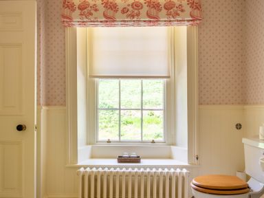 A bathroom window with a roll blind and floral valance above a radiator and beside a toilet with a wooden seat at Silverholme in Graythwaite near Hawkshead