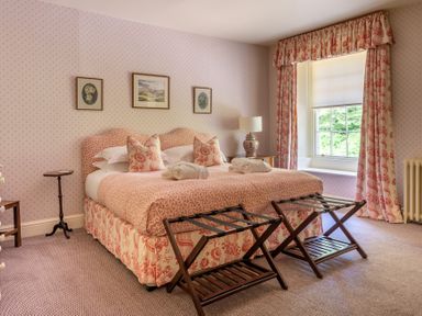 A bedroom with a double bed two luggage racks and a window with curtains at Silverholme in Graythwaite near Hawkshead