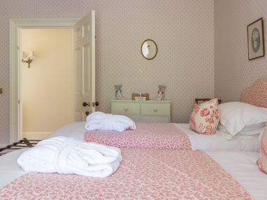 A bedroom with two single beds with pink patterned bedding and white robes on top at Silverholme Graythwaite near Hawkshead