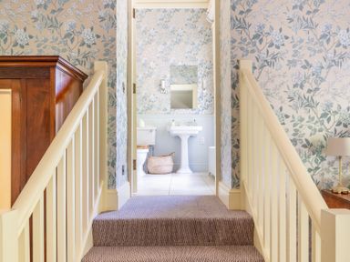 A stairway with beige railings leading to a bathroom with floral wallpaper a pedestal sink and a toilet at Silverholme Graythwaite near Hawkshead