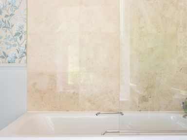 A bathroom with a bathtub tiled wall a glass shower screen and floral wallpaper at Silverholme in Graythwaite near Hawkshead
