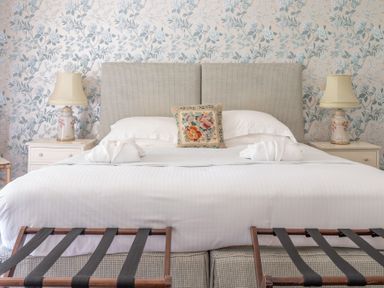 A bed with white bedding two bedside tables with lamps and floral wallpaper at Silverholme Graythwaite near Hawkshead