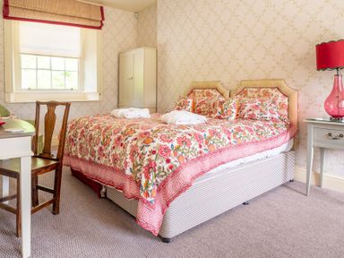 A bedroom with a double bed with floral bedding a wooden chair and a table with a pink lamp at Silverholme Graythwaite near Hawkshead