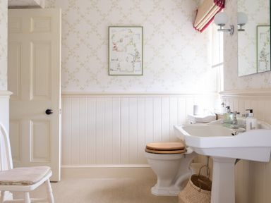 A bathroom with a toilet with a wooden seat a pedestal sink and a white chair at Silverholme Graythwaite near Hawkshead