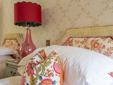 A bedroom with floral patterned pillows on a bed and a red lamp on a bedside table at Silverholme in Graythwaite near Hawkshead
