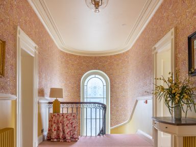 A hallway with patterned wallpaper a window with decorative glass a table with a lamp and a side table with flowers at Silverholme Graythwaite near Hawkshead