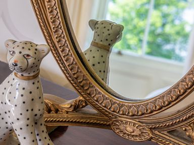 A ceramic cheetah figurine in front of an ornate oval mirror with a window and greenery reflected in the glass at Silverholme in Graythwaite near Hawkshead