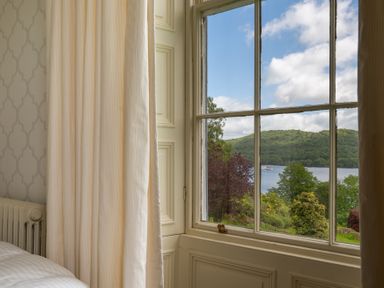 A window with curtains overlooking trees and a lake at Silverholme Graythwaite near Hawkshead