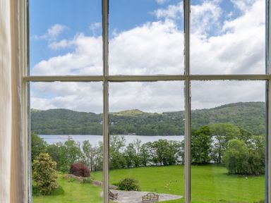 A window view of a garden with trees and benches overlooking a lake and hills at Silverholme Graythwaite near Hawkshead
