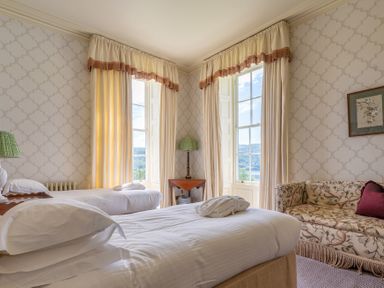 A bedroom with two single beds a patterned sofa and large windows with curtains at Silverholme in Graythwaite near Hawkshead