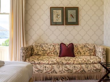 A patterned sofa with a red pillow under two framed bird pictures in a room with patterned wallpaper at Silverholme in Graythwaite near Hawkshead