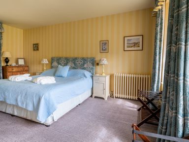 A bedroom with a bed covered in blue bedding next to white nightstands and a wooden dresser at Silverholme in Graythwaite near Hawkshead