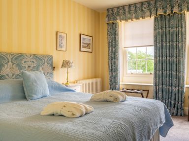 A bedroom with a large bed covered with a blue bedspread and two folded white robes on top at Silverholme in Graythwaite near Hawkshead
