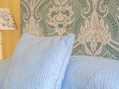 A close-up of a light blue quilted pillow and bedspread with a patterned fabric headboard and a lamp in the background at Silverholme Graythwaite near Hawkshead