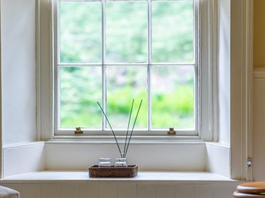 A window with a white frame and a basket holding two glass containers with reed sticks on the windowsill at Silverholme in Graythwaite near Hawkshead