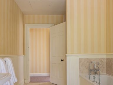A bathroom with a bathtub and a partially open door showing a hallway at Silverholme Graythwaite near Hawkshead