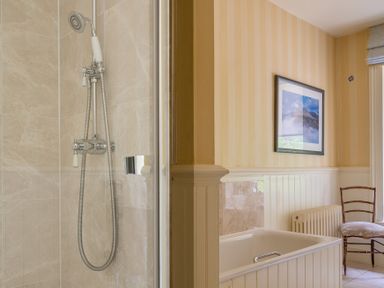 A bathroom with a shower area beside a bathtub a wooden chair and a framed picture on the wall at Silverholme in Graythwaite near Hawkshead