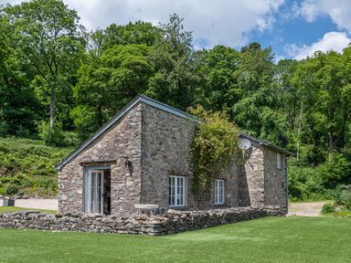 A stone cottage with white window frames surrounded by grass and trees at Silverholme in Graythwaite near Hawkshead