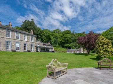 A large stone house with a lawn and wooden benches on a patio at Silverholme Graythwaite near Hawkshead