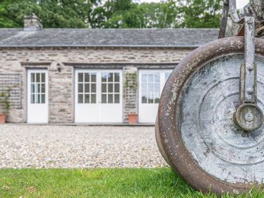 A stone building with three white doors and a gravel driveway and a close up of a rusted metal wheel in the foreground at Silverholme Graythwaite near Hawkshead