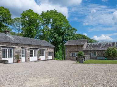 A gravel courtyard with stone buildings and trees in the background at Silverholme in Graythwaite near Hawkshead