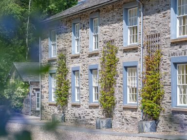 Stone building with blue window frames and climbing plants on trellises in containers at Silverholme in Graythwaite near Hawkshead
