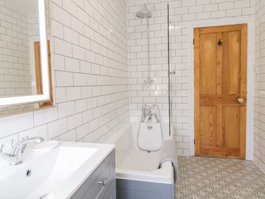 A bathroom with a bathtub shower sink mirror tiled walls and a wooden door at Cooper's Rest Gorffwysfa Coopers in Dolwyddelan