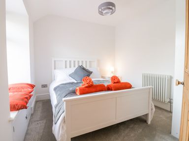A bedroom with a white bed frame a grey blanket orange towels and two orange pillows at Cooper's Rest Gorffwysfa Coopers in Dolwyddelan