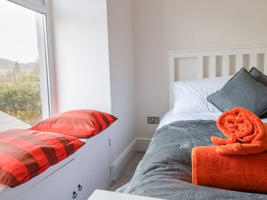 A bed with white and grey bedding and orange towels next to a window seat with red cushions at Cooper's Rest Gorffwysfa Coopers in Dolwyddelan