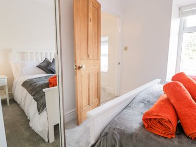A bedroom with a white bed frame gray bedding orange towels on the bed a wooden door and a window at Cooper's Rest Gorffwysfa Coopers in Dolwyddelan