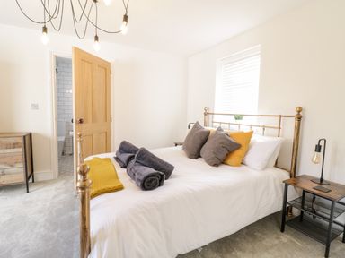 A bedroom with a gold metal bed frame pillows and towels on the bed a wooden door an open door to a bathroom a wooden dresser and two bedside tables at Coopers Rest Gorffwysfa Coopers in Dolwyddelan
