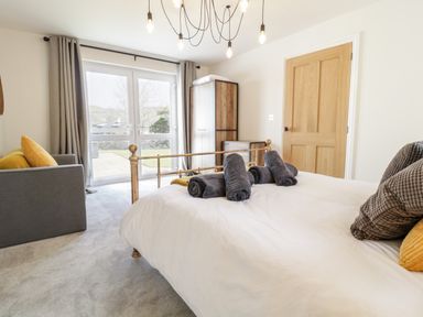 A bedroom with a bed and gray rolled towels next to a wooden door and glass doors at Cooper's Rest Gorffwysfa Coopers in Dolwyddelan