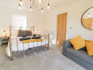 A bedroom with a metal bed frame pillows and folded towels a gray sofa with yellow cushions and a round mirror at Cooper's Rest Gorffwysfa Coopers in Dolwyddelan