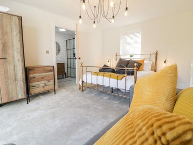 A bedroom with a brass bed frame, wooden dresser, and yellow cushions at Cooper's Rest in Dolwyddelan