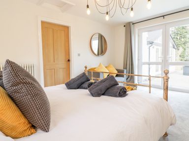 A bedroom with a metal bed, pillows, towels, a door, a mirror, a small sofa, and glass doors at Cooper's Rest Gorffwysfa Coopers in Dolwyddelan