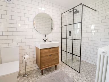 A bathroom with a toilet sink wooden vanity round mirror and glass shower at Coopers Rest Gorffwysfa Coopers in Dolwyddelan