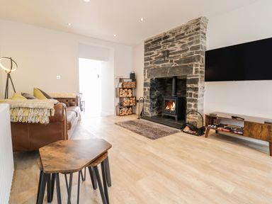 A living room with a leather sofa wood burning stove and a wall mounted television at Cooper's Rest Gorffwysfa Coopers in Dolwyddelan