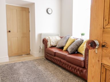 A room with a brown leather sofa with cushions and a wooden door at Cooper's Rest Gorffwysfa Coopers in Dolwyddelan