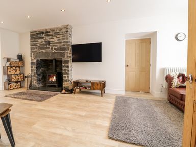 A living room with a stone fireplace a wall-mounted TV a wooden storage unit a brown leather sofa and wood stacked on shelves at Cooper's Rest in Dolwyddelan